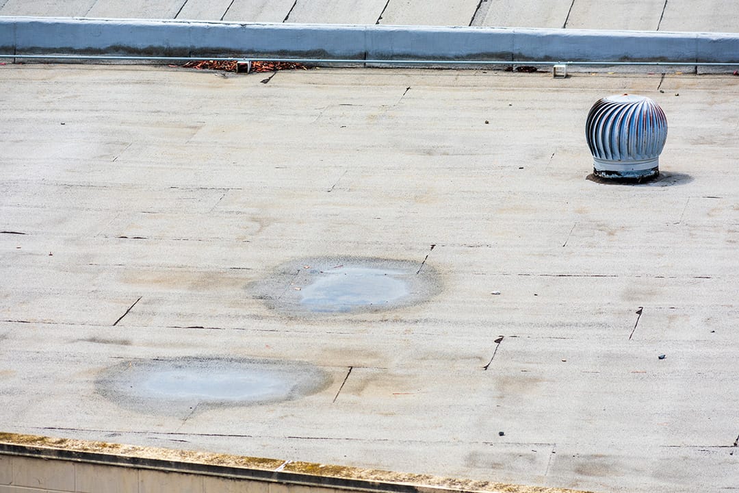 Ponding water on the settled flat roof. Turbine vent on the flat roof in an industrial building.