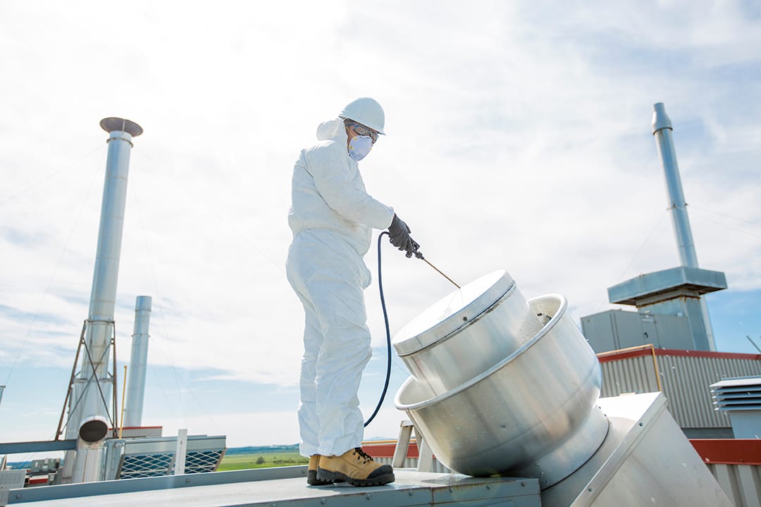 A professional in protective uniform, mask, gloves in the roof for cleaning. Winter Prep for Commercial Roofs.