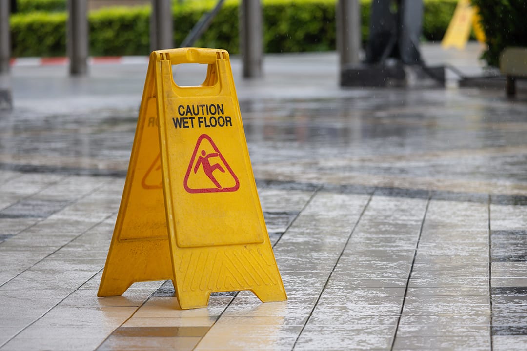 A yellow caution sign is on the ground in front of a building