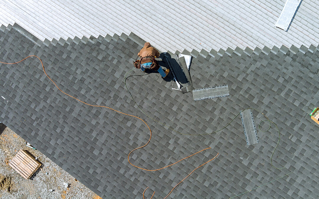 A asphalt shingles installation on the commercial roof roofer is nailing asphalt shingles to roofing construction