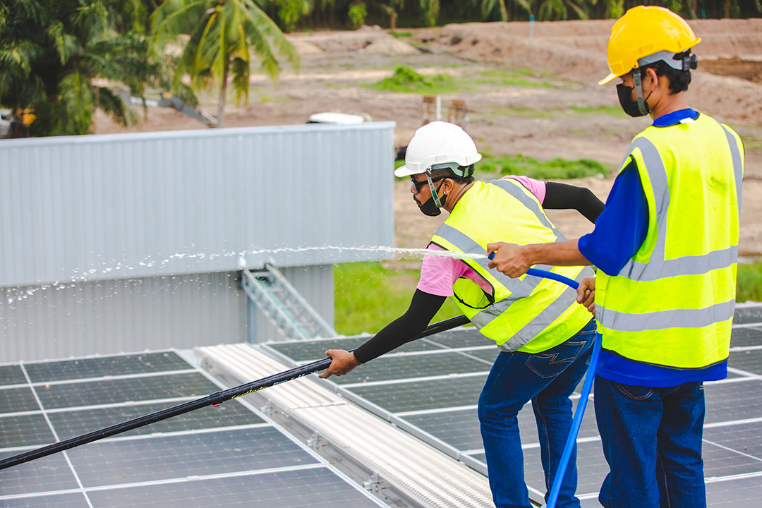 Professional worker cleaning solar panels with brush and washing with water on roof structure - Steps of a Flat Roof Replacement