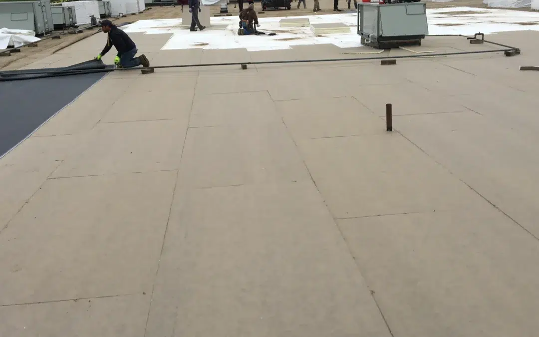Workers installing roofing materials on a large flat rooftop.